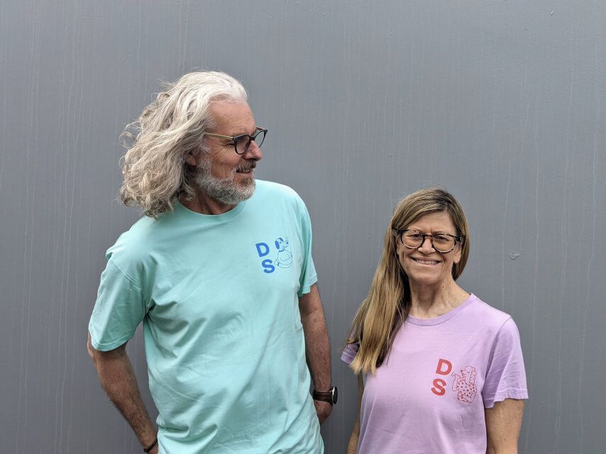 A man, Peter, in a blue Dog Street T-shirt and a woman, Julie, in a purple Dog Street T-shirt. 